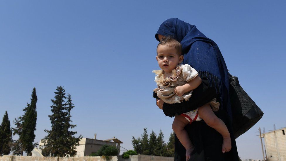 A Syrian woman holds her child walks at the Abu Duhur crossing on the eastern edge of Idlib province