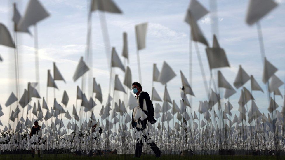 A man in a mask walks among flags representing those that died from Covid