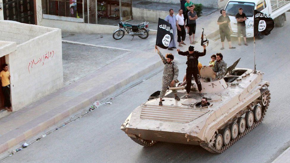 IS militants hold up black jihadist banners in Raqqa on 30 June 2014