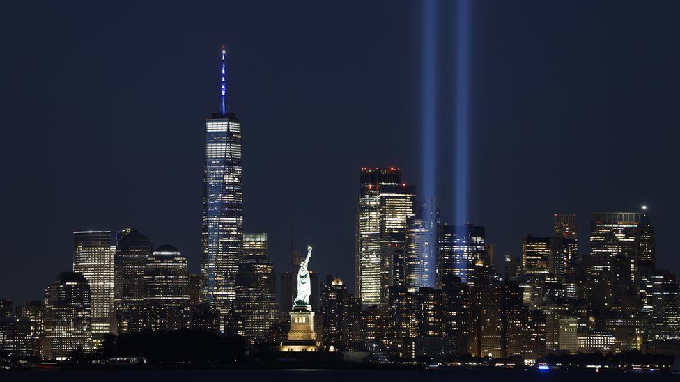 The Tribute in Light is illuminated behind the Statue of Liberty and next to One World Trade Center in New York City on the 20th anniversary of the 9/11 attacks