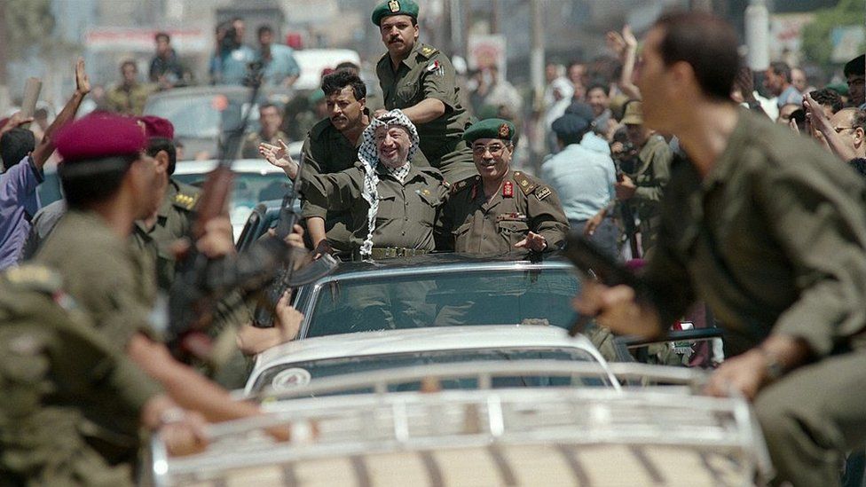 Председатель ООП Ясир Арафат в окружении телохранителей приветствует ликующую толпу палестинцев во время своего тура по городу Газа (07.03.04)