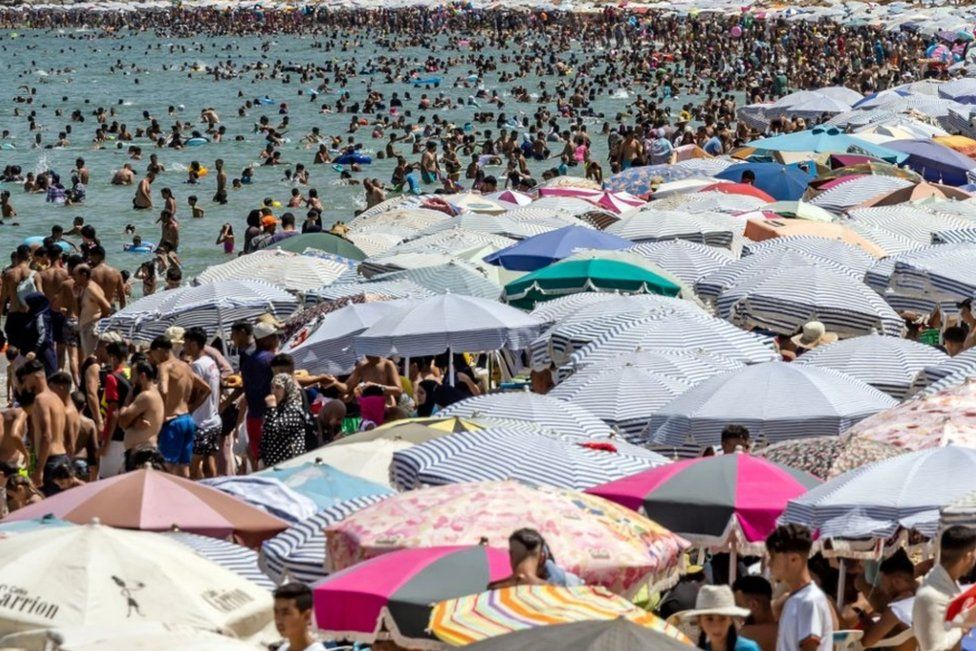 Thousands on a beach with many umbrellas, 30 July 2023