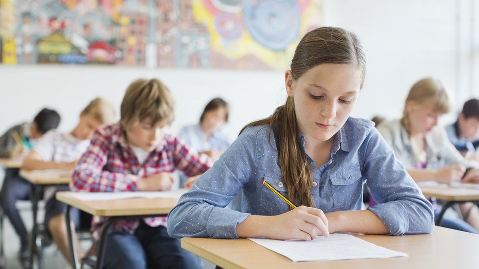 A group of students, dressed in their own clothes, doing a test in a classroom setting