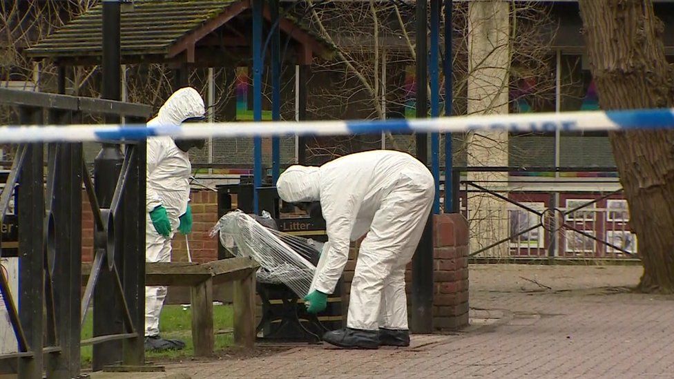 Forensics officers in protective clothing wrap clingfilm around a bench