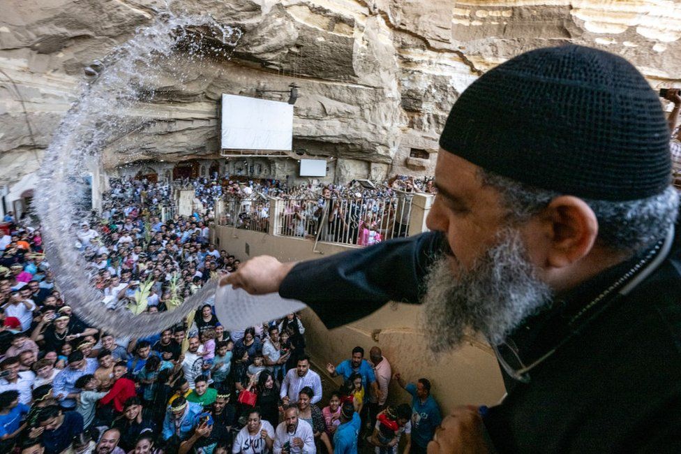 Coptic Orthodox priest sprinkles holy water on gathering worshippers.