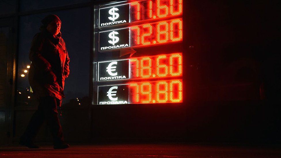 A woman walks past a board listing foreign currency rates against the Russian ruble in central Moscow