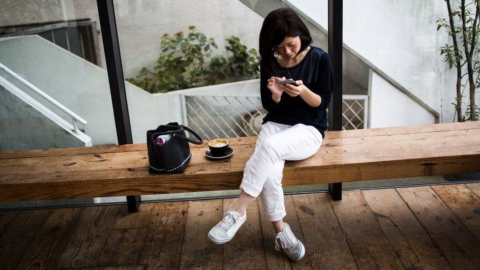 woman checking phone sitting on a bench, wearing sneakers