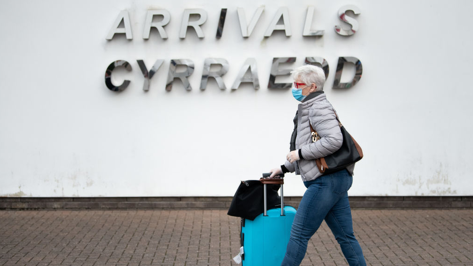 Woman with suitcase walking past arrivals sign at Cardiff Airport