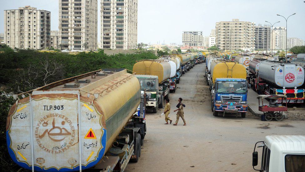 Pakistani men walk past fuel tankers, used to transport fuel to NATO forces in Afghanistan, parked near oil terminals in Pakistan's port city of Karachi on May 16, 2012