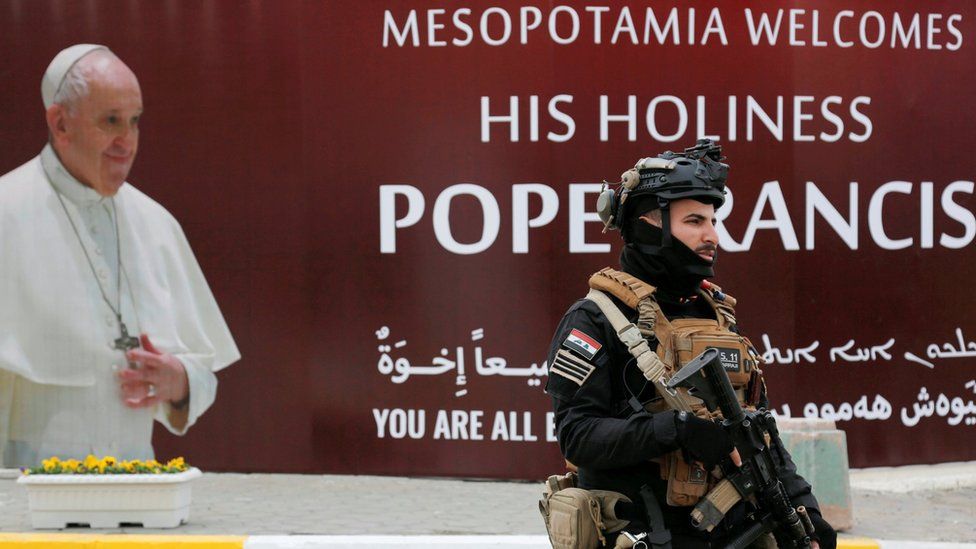 Офицер службы безопасности идет возле плаката с изображением Папы Франциска в Багдаде перед его визитом в Ирак (4 марта 2021 г.)