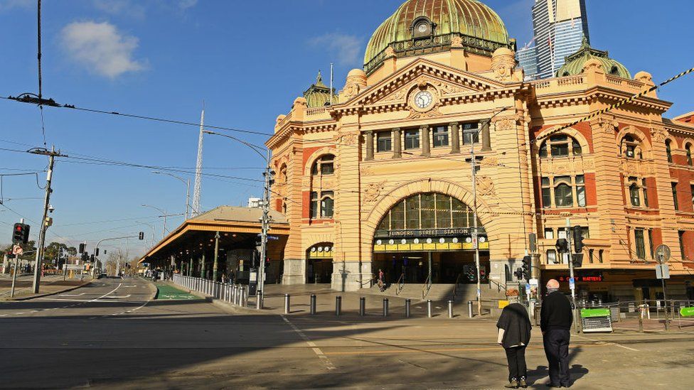 Two people stand in front of an otherwise deserted Flinders St Station in Melbourne