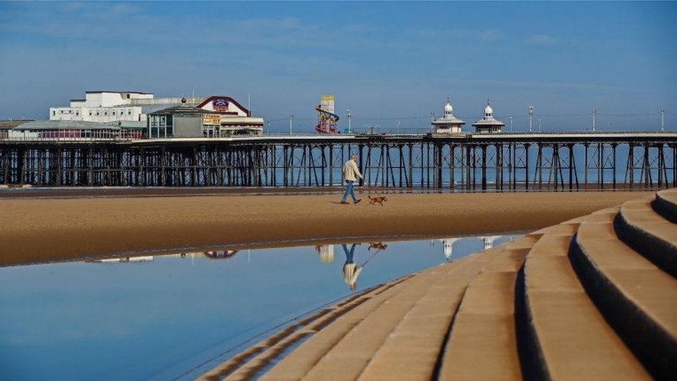 A man walks his dog along Blackpool beach in the sunshine
