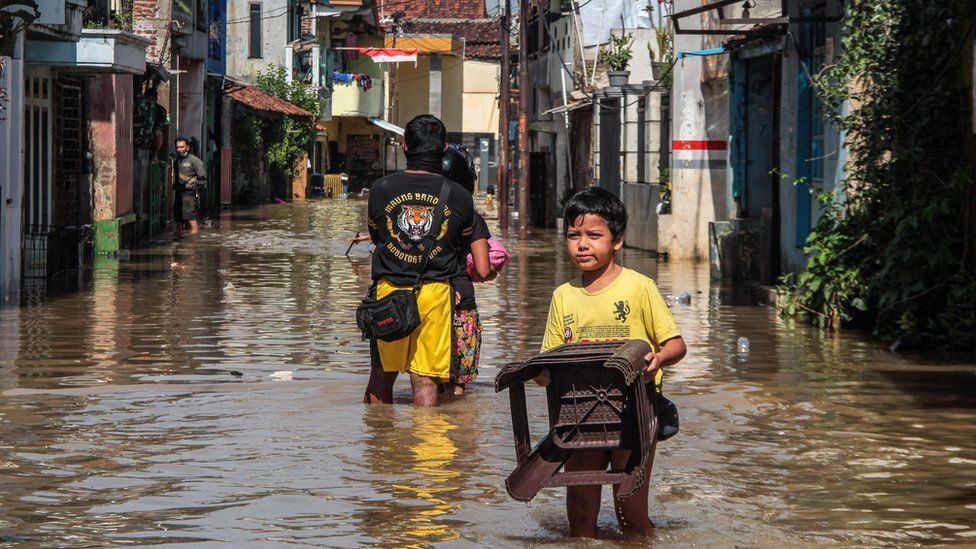 Мальчик со стулом идет по затопленной дороге в Индонезия