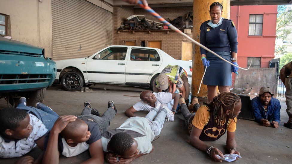 Suspects lie on floor as a member of the South African Police Service (SAPS) arrests them because they defied the lockdown rules and was found with alcohol in Hillbrow, Johannesburg, on March 27, 2020