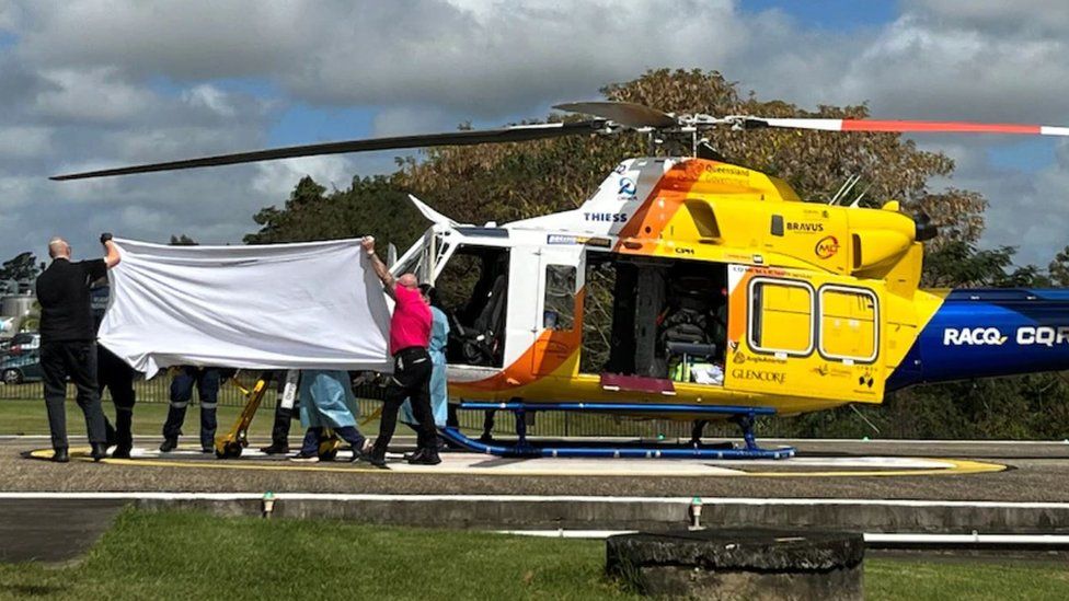 A person on a stretcher is covered with a white sheet near a helicopter