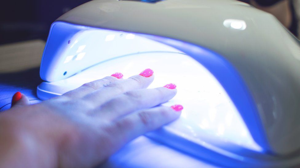 Female Hand with red nails in the lamp for manicure. Nail Lamp Dryer for Gel Nail Polish Curing Manicure Pedicure.
