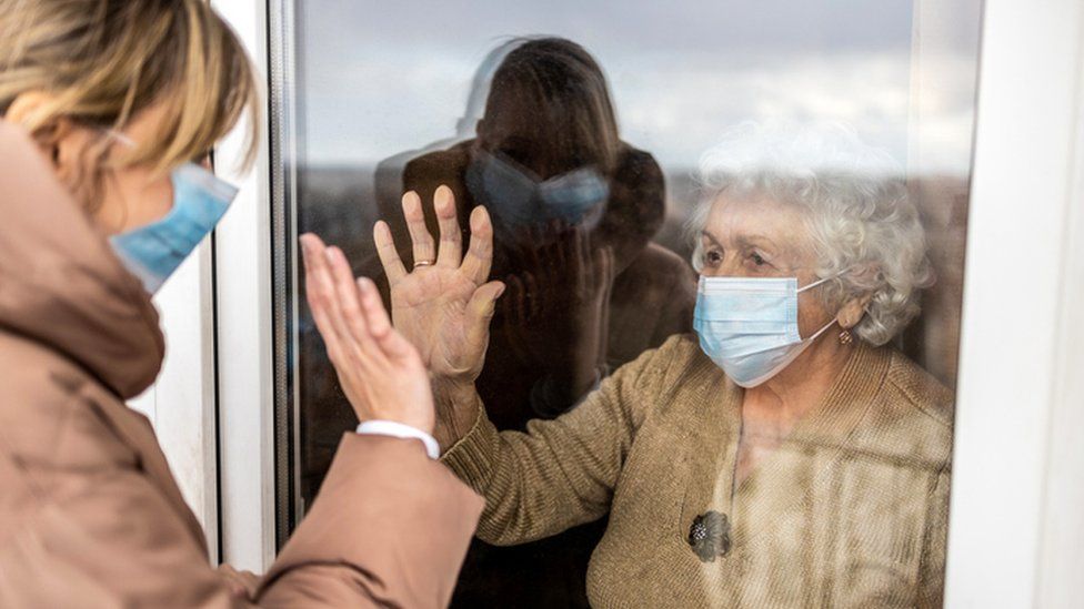 Woman visiting an elderly relative at a care home during the coronavirus pandemic and having to wave from outside
