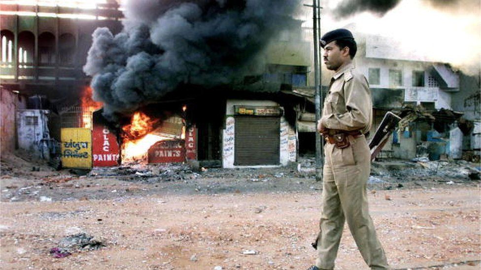 In this picture taken 01 March 2002, An Indian policeman looks on as a row of shops burns in Ahmedabad.