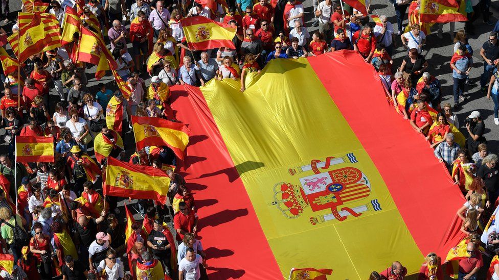 Image shows protesters holding a giant Spanish flag during a demonstration to support the unity of Spain on 8 October 2017