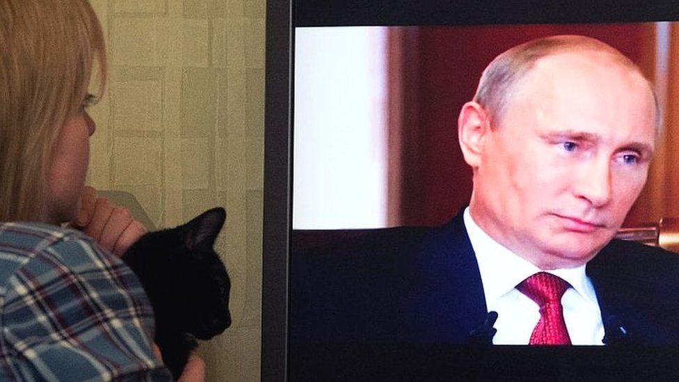 A woman looks at Russian President Vladimir Putin on a screen