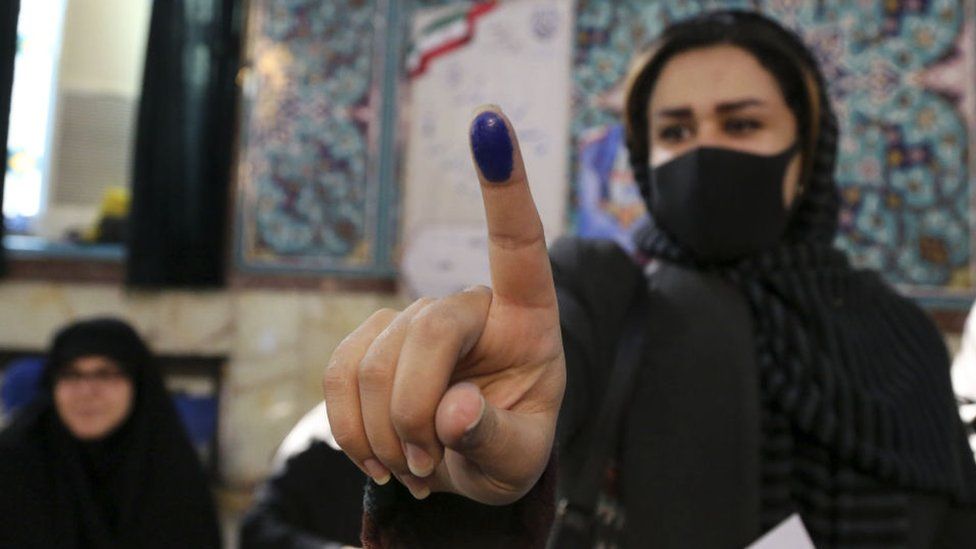 A woman wearing a face mask shows her ink-marked finger after casting ballot in the Iranian election