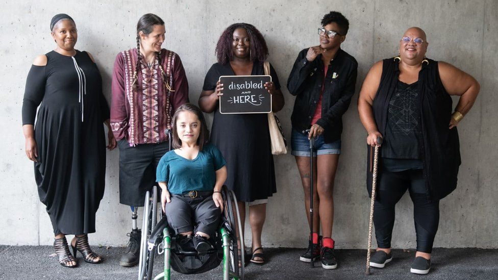 Collection of women holding a 'Disabled and here' sign