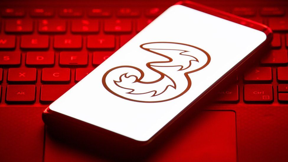 The Three mobile logo on a phone on top of a keyboard, lit in red glow from the screen