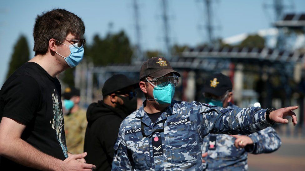 A member of the Australian air force stands next to a man wearing a face mask