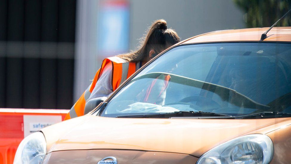 CARDIFF, WALES, UNITED KINGDOM - SEPTEMBER 09, 2020 - A woman wearing a high-visibility jacket consults with a motorist at the drive-through coronavirus test centre at Cardiff City Stadium as new cases of the virus rise across the UK