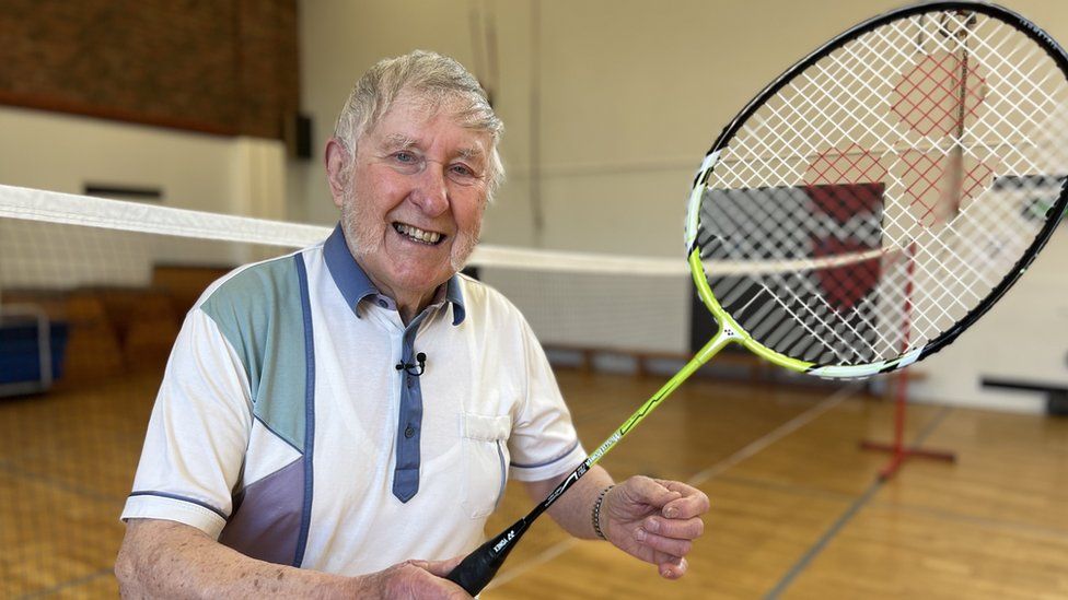Colin Bedford holds his racket aloft on a badminton court