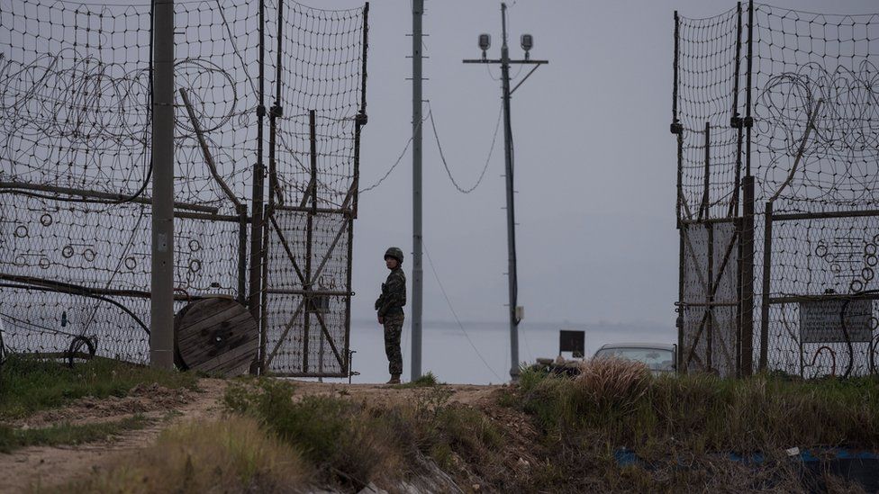 A soldier stands guard at an opening in a fence at the DMZ
