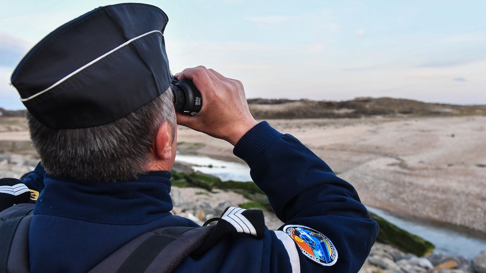 A French Gendarme looks through a pair of binoculars during a patrol of the beaches at Tardinghen near the northern port city of Calais on April 4, 2019