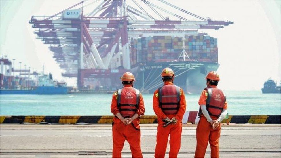 Dock workers in China watch a container ship