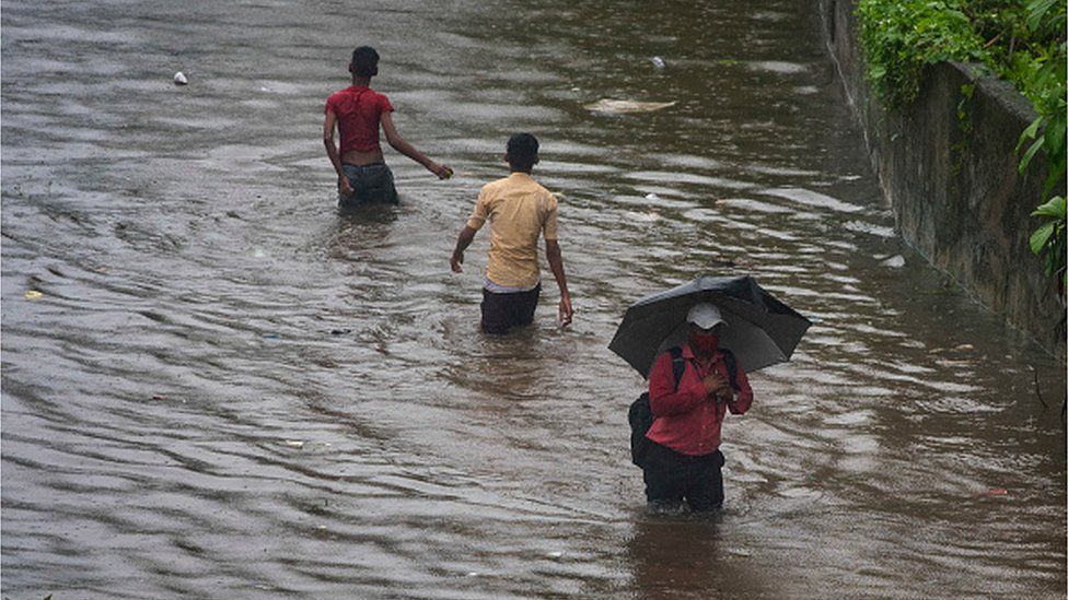 People wade through waterlogged road due to heavy rain at Tilak Nagar Station on July 5, 2022 in Mumbai, India.