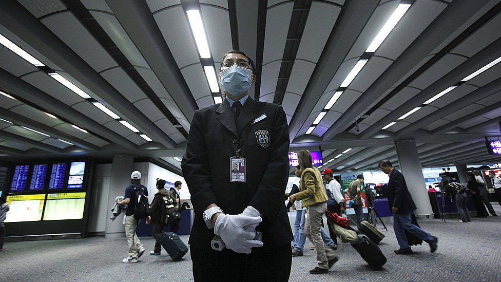 A health worker stands by ready to ask passengers to remove head gear prior to temperature screening on April 27, 2009 at the international airport in Hong Kong