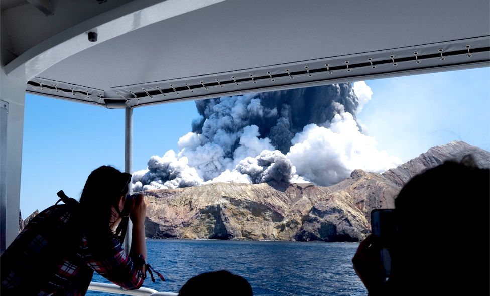 Tourists on a boat witnessing and taking photos of the volcano on New Zealand's White Island as it spews steam and ash
