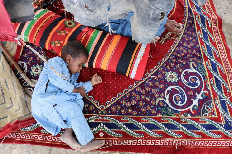 A boy takes a nap while lying on a carpet and sheltering from the sun.