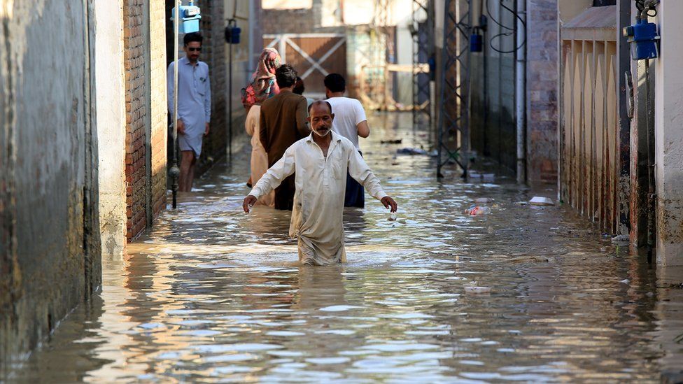 Image shows man wading through flooded street