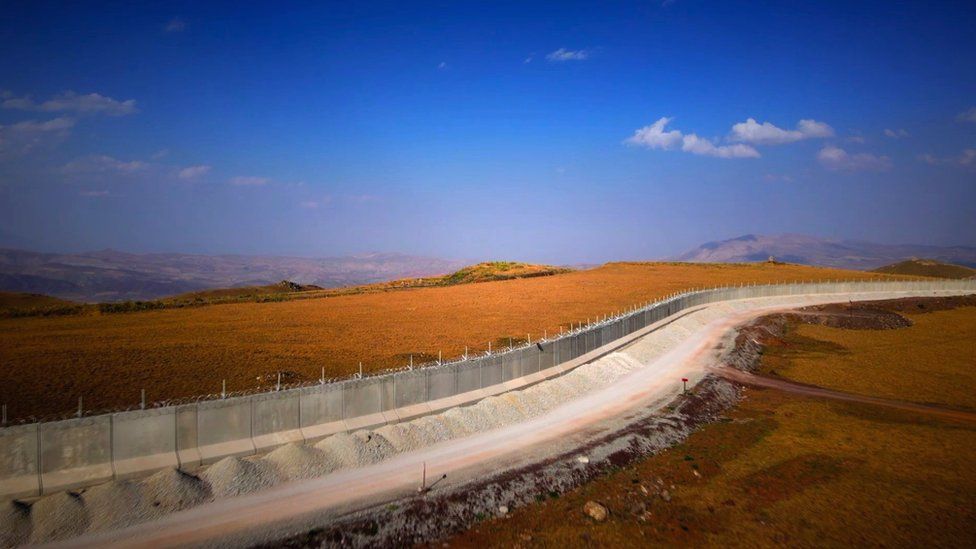 Concrete border wall runs along landscape with blue sky above