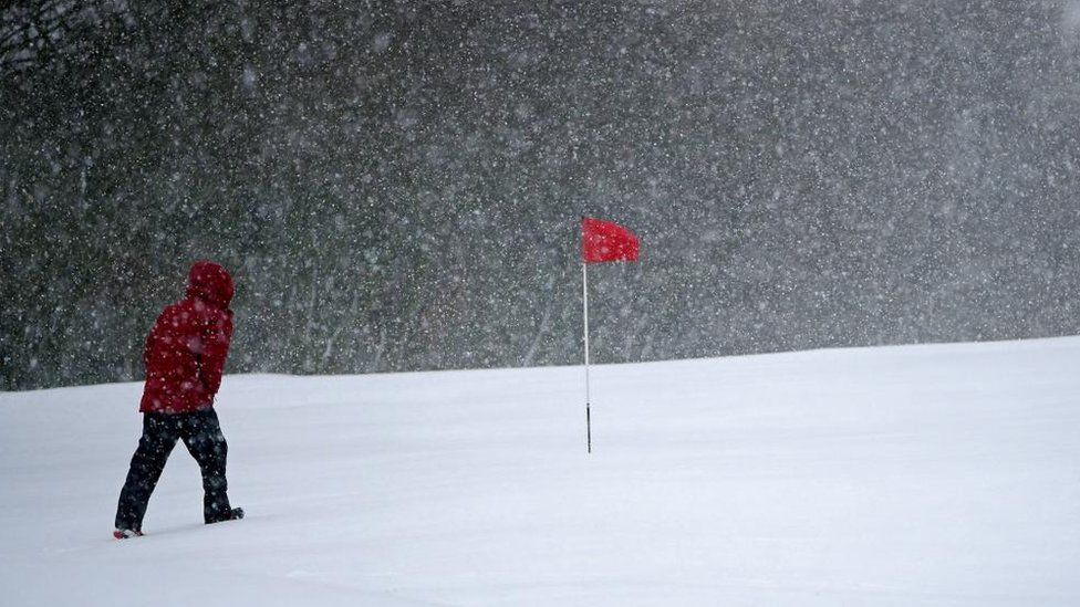A man walking over a golf course in heavy snow
