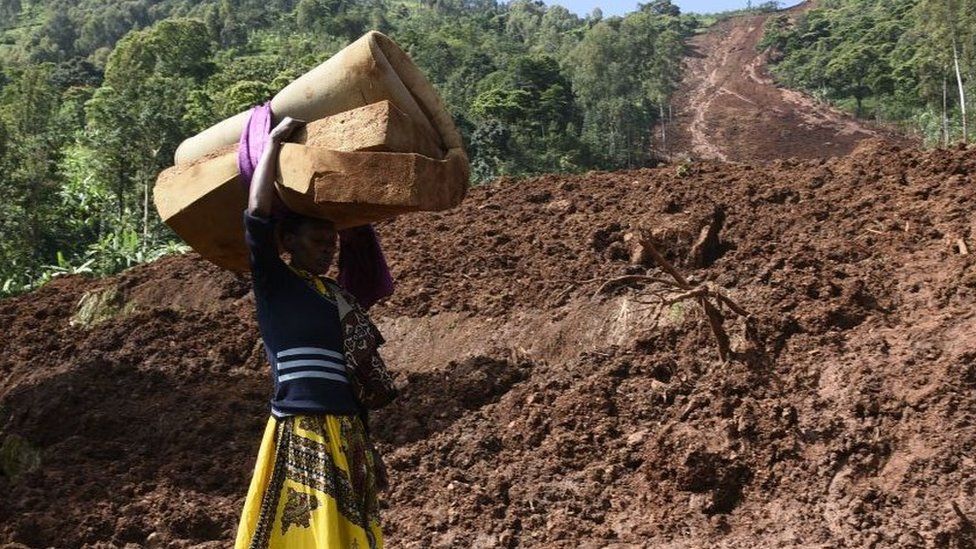 A woman carries a rolled-up mattress at a landslide site in Shisakali village of Bududa district, eastern Uganda,