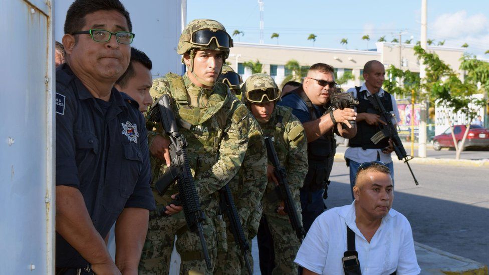 Policemen and soldiers take cover at the place where a shooting erupted ensuing an attack against the building of the Quintana Roo State Prosecution, in Cancun, Mexico