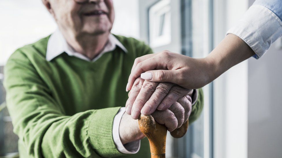 Close-up of woman holding senior man's hand leaning on cane - stock photo