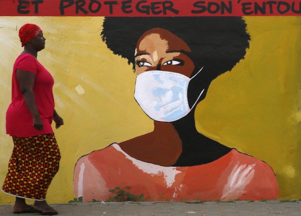 People pass a mural painted on a wall meant to sensitize the locals on how to prevent themselves from contracting and spreading the COVID-19 coronavirus, in Abidjan, Ivory Coast, 22 October 2020.