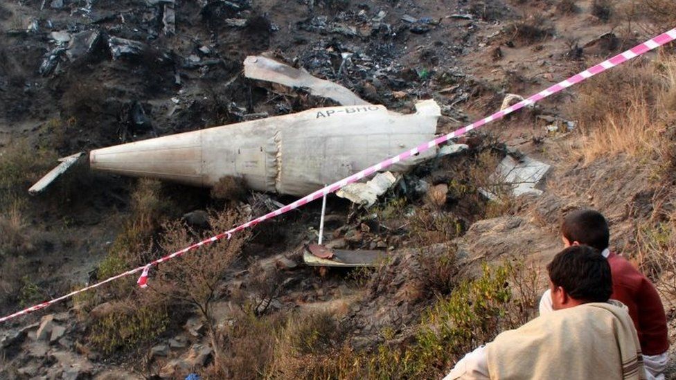 巴基斯坦国际航空公司一架涡轮螺旋桨客机在巴基斯坦哈维连附近坠毁后，当地居民坐在残骸旁（2016 年 12 月 8 日）