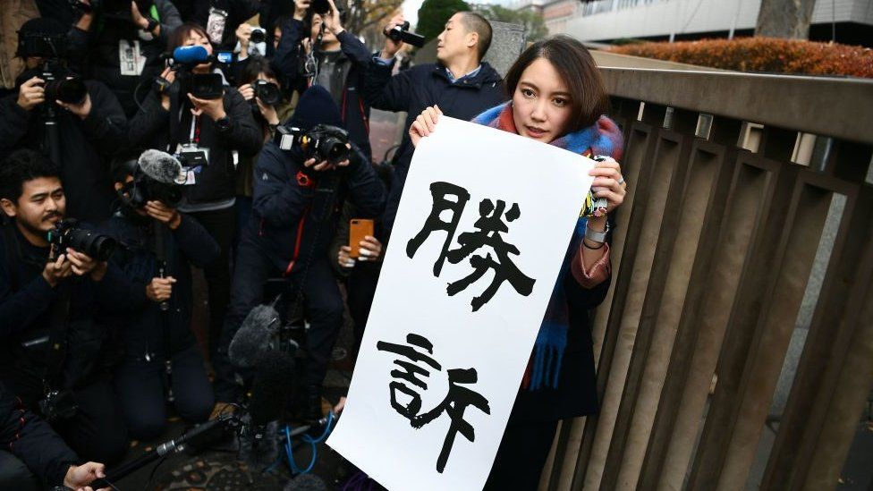 Shiori Ito holds up a sign saying "victory"