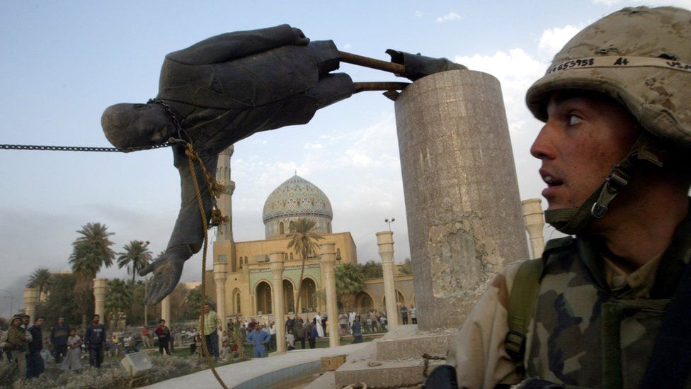 A US soldier watches as a statue of ousted Iraqi President Saddam Hussein is pulled over in Baghdad, Iraq (9 April 2003)