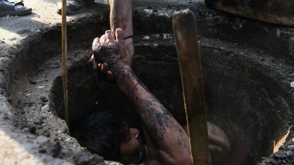 An Indian manual scavenger is helped out of a manhole in the old quarters of New Delhi on March 21, 2018. Slum dwellers depend on government supplies for drinking water and struggle to get adequate supply during summers. World Water Day is observed on March 22 and focuses on the importance of universal access to clean water, sanitation and hygiene facilities. / AFP PHOTO / CHANDAN KHANNA (Photo credit should read CHANDAN KHANNA/AFP via Getty Images)