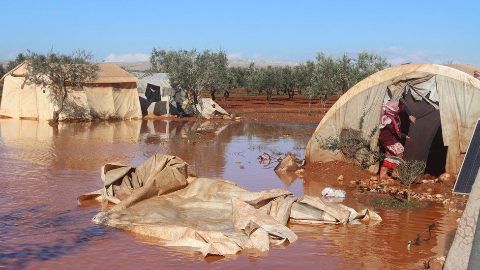 A woman stands in her flooded tent in Idlib province, Syria