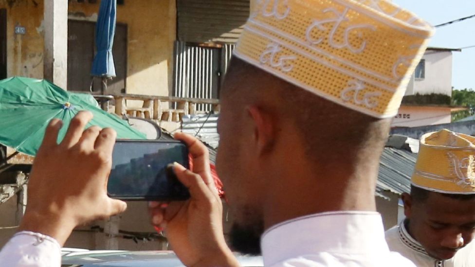 A Comorian man in a kofia hat taking a photo